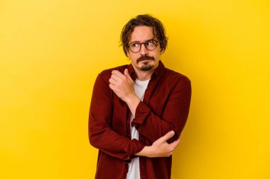 Sarı arka planda izole edilmiş genç beyaz adam şaşkın, şüpheli ve güvensiz hissediyor..