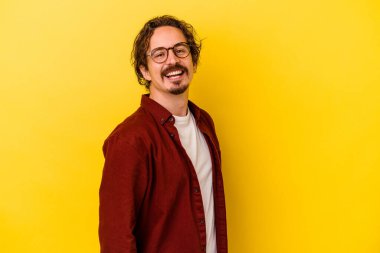 Sarı arka planda izole edilmiş genç beyaz adam ellerini kalçalarına koyuyor..