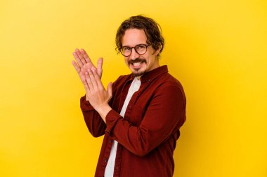 Sarı arka planda izole edilmiş genç beyaz adam enerjik ve rahat hissediyor, ellerini ovuşturuyor kendinden emin..