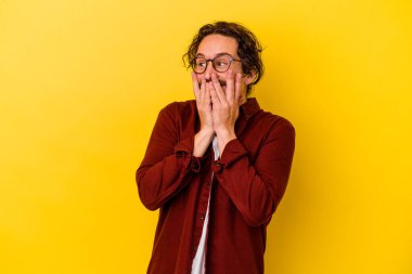 Sarı arka planda izole edilmiş genç beyaz bir adam bir şeye gülüyor, ağızlarını ellerle kapatıyor..