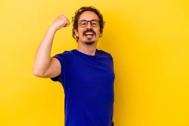 Sarı arka planda izole edilmiş genç beyaz adam tasasız ve heyecanlı bir şekilde tezahürat yapıyor. Zafer konsepti.