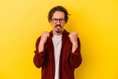 Sarı arka planda izole edilmiş genç beyaz adam kameraya yumruk gösteriyor, agresif yüz ifadesi var..