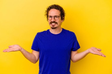 Sarı arka planda izole genç beyaz adam kollarıyla ölçek yapar, mutlu ve kendinden emin hisseder..