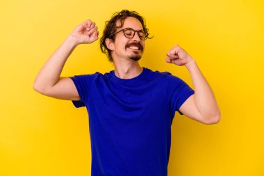 Sarı arka planda izole edilmiş genç beyaz adam özel bir günü kutluyor, atlıyor ve enerjiyle kollarını kaldırıyor..