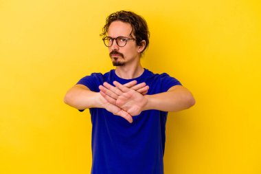 Sarı arka planda izole edilmiş genç beyaz adam inkar jesti yapıyor.