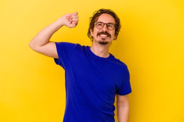 Sarı arka planda izole edilmiş genç beyaz adam zaferi, tutkuyu ve coşkuyu kutluyor, mutlu bir ifade..