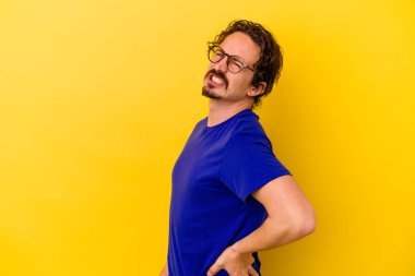 Sarı arka planda izole edilmiş beyaz bir adam sırt ağrısı çekiyor..