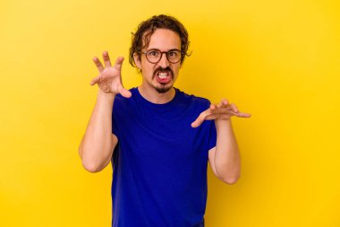 Sarı arka planda izole edilmiş genç beyaz adam pençelerini kedi taklidi yaparken gösteriyor, agresif bir hareket..