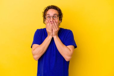 Sarı arka planda izole edilmiş genç beyaz adam şok olmuş, ağzı ellerle kaplanmış, yeni bir şey keşfetmeye hevesli..