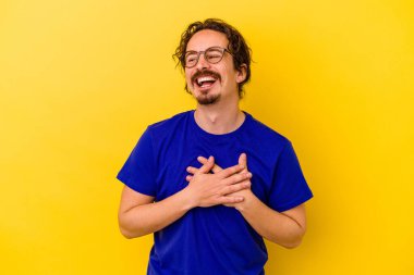 Sarı arka planda izole olmuş genç beyaz adam gülüyor, elini yüreğine koyuyor, mutluluk kavramını koruyor..