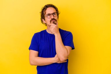 Kafkasyalı genç adam sarı arka planda izole edilmiş düşünüyor ve yukarı bakıyor, yansıtıyor, düşünüyor, hayal kuruyor..