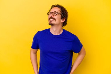 Sarı arka planda izole edilmiş genç beyaz adam gevşemiş ve mutlu gülüyor, boynunda dişlerini gösteriyor..