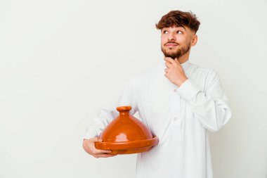 Tipik Arap kostümü giyen genç Faslı bir adam beyaz arka planda izole edilmiş, şüpheli ve şüpheci bir ifadeyle yana bakıyor..