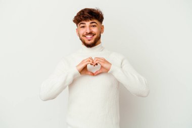 Beyaz arka planda izole edilmiş genç Faslı adam gülümsüyor ve elleriyle kalp şekli gösteriyor..