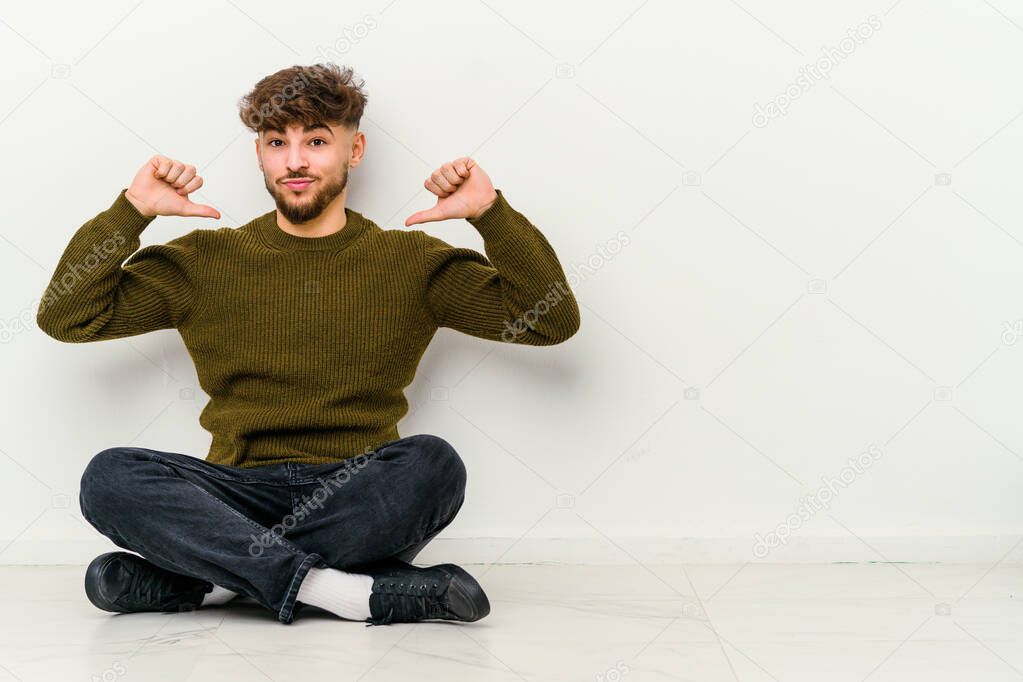 Young Moroccan man sitting on the floor isolated on white background feels proud and self confident, example to follow.