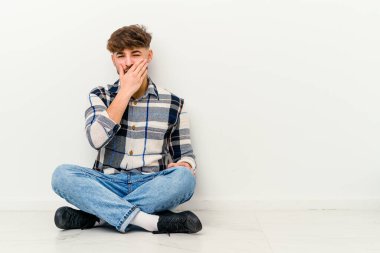 Genç Faslı bir adam beyaz arka planda izole bir şekilde yerde oturmuş gülerek, kaygısızca, doğal duygularla gülüyor..