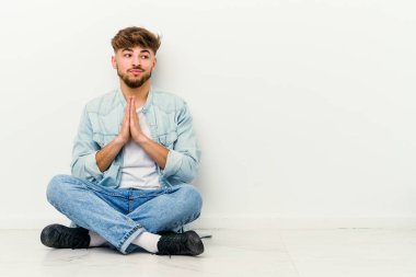 Genç Faslı bir adam beyaz arka planda yalnız başına oturmuş dua ediyor, kendini adamış, ilahi ilhamı arayan dindar biri..