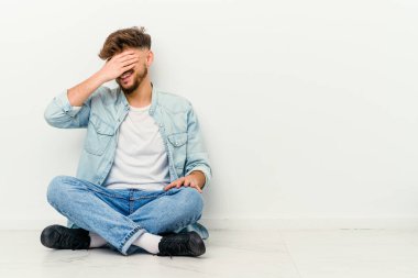 Beyaz arka planda izole bir şekilde yerde oturan genç Faslı adam ellerini başının üstünde tutarak neşeyle gülüyor. Mutluluk kavramı.