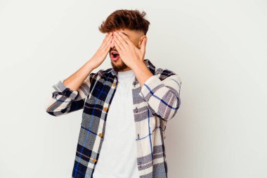 Faslı genç bir adam beyaz arka planda izole edilmiş, elleriyle gözlerini kapatmaktan korkuyor..