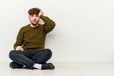 Beyaz arka planda izole bir şekilde yerde oturan Faslı genç adam şoka uğruyor, önemli bir toplantı hatırladı..