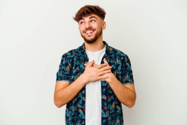 Genç Faslı bir adam beyaz arka planda izole edilmiş. Gülüyor, elini yüreğine koyuyor, mutluluk kavramını koruyor..