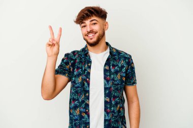 Beyaz arka planda izole edilmiş genç Faslı adam neşeli ve kaygısız parmakları olan bir barış sembolü gösteriyor..
