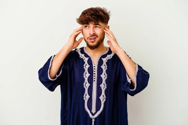 Young Moroccan man isolated on white background covering ears with fingers, stressed and desperate by a loudly ambient.