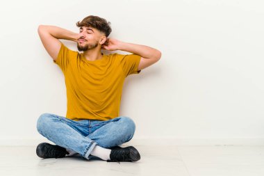 Genç Faslı bir adam beyaz arka planda izole bir şekilde yerde oturuyor. Oturma düzeninden dolayı boyun ağrısı çekiyor..