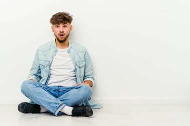 Beyaz arka planda izole bir şekilde yerde oturan Faslı genç adam gördüğü bir şey yüzünden şoka uğruyor..