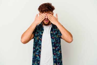 Faslı genç bir adam beyaz arka planda izole edilmiş, elleriyle gözlerini kapatmaktan korkuyor..