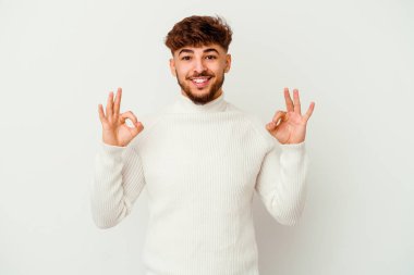 Genç Faslı bir adam beyaz arka planda izole edilmiş neşeli ve kendinden emin bir şekilde iyi bir jest yapıyor..