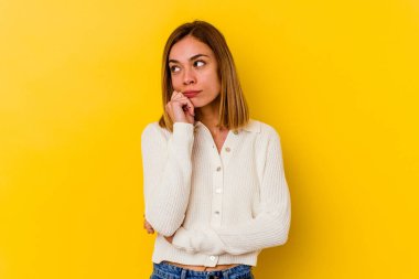 Beyaz tenli genç bir kadın sarı arka planda izole edilmiş düşünüyor ve yukarı bakıyor, yansıtıyor, düşünüyor, hayal kuruyor..