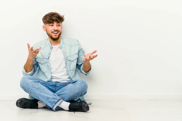 Joven Hombre Marroquí Sentado Suelo Aislado Sobre Fondo Blanco Alegre —  Fotos de Stock