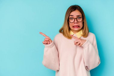Mavi arka planda izole edilmiş genç beyaz kadın işaret parmağıyla fotokopi alanını işaret ederek şok oldu..