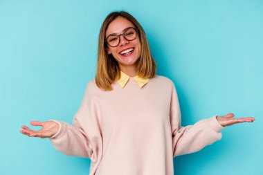 Mavi arka planda izole edilmiş genç beyaz kadın hoş bir ifade sergiliyor..