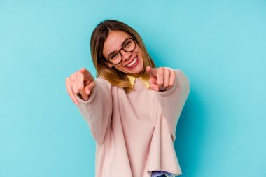 Genç beyaz kadın, mavi arka planda izole edilmiş. Önü işaret eden neşeli gülümsemeler..