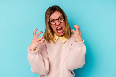 Mavi arka planda izole edilmiş genç beyaz kadın gergin elleriyle çığlık atıyor..