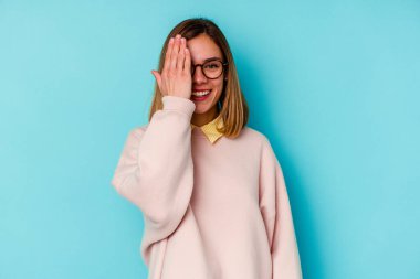 Mavi arka planda izole edilmiş genç beyaz kadın yüzünün yarısını palmiye ile örterek eğleniyor..