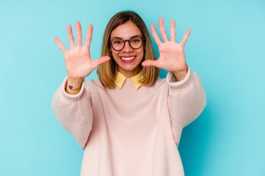 Mavi arka planda izole edilmiş genç beyaz kadın on numarayı elleriyle gösteriyor..