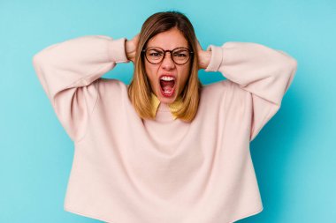 Kafkasyalı genç bir kadın mavi arka planda izole edilmiş kulakları kulaklarıyla kapatıyor ve çok ses duymamaya çalışıyor..