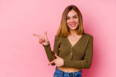 Pembe arka planda izole edilmiş genç beyaz kadın işaret parmaklarıyla işaret ederek heyecanlanıyor..