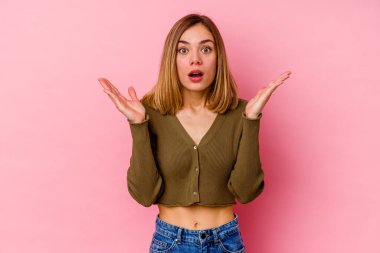 Pembe arka planda izole edilmiş genç beyaz kadın şaşırmış ve şok olmuş..