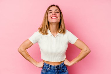 Pembe arka planda izole edilmiş beyaz bir kadın. Kendine güveni tam. Kalçalarını tutuyor..