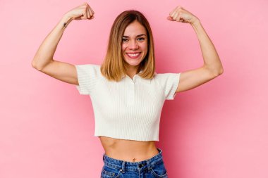 Pembe arka planda izole edilmiş genç beyaz kadın güçlü bir hareket gösteriyor. Kollarıyla, kadınsı gücün sembolü.