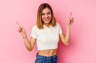 Pembe arka planda izole edilmiş genç beyaz kadın farklı kopya alanlarını gösteriyor, birini seçiyor, parmağıyla gösteriyor..