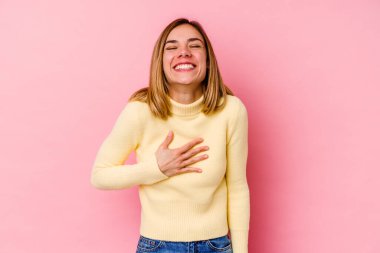 Pembe arka planda soyutlanmış beyaz bir kadın yüksek sesle gülüyor ve elini göğsüne koyuyor..