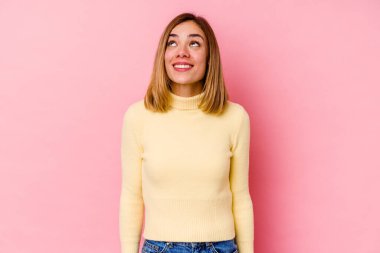 Genç beyaz kadın pembe arka planda izole edilmiş rahat ve mutlu bir şekilde gülüyor, boynunda dişlerini gösteriyor..