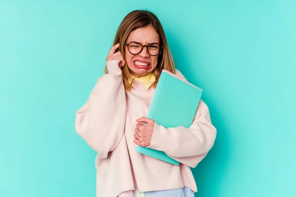 Joven Estudiante Sosteniendo Libros Aislados Sobre Fondo Azul Cubriendo Orejas —  Fotos de Stock