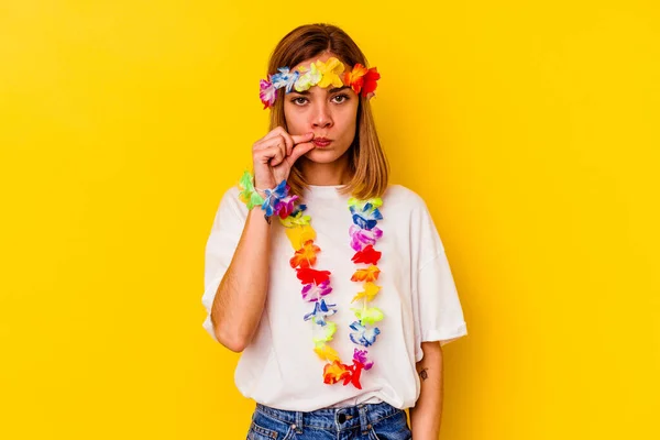 若いですCaucasian女性祝いますA Hawaiianパーティー孤立した上に黄色の背景に指で唇を保ちます秘密 — ストック写真