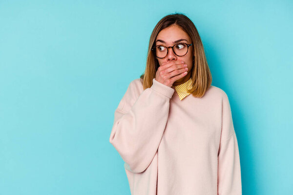 Молодая студентка кавказская женщина изолирована на синем фоне вдумчивый глядя на пространство для копирования покрывая рот рукой.